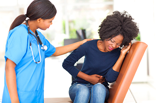 A woman holds her stomach in pain as a doctor comforts her.