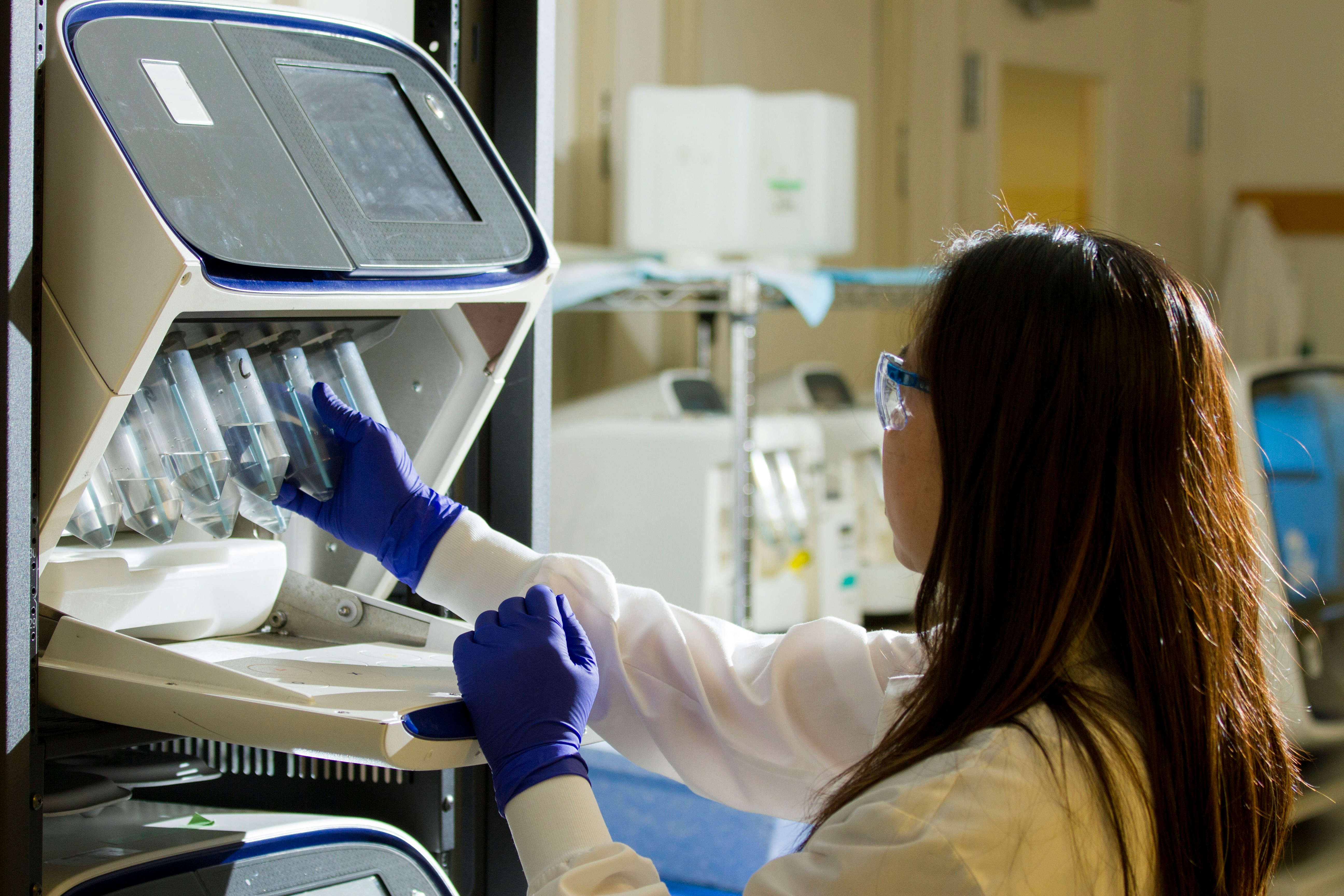 Dark haired person wearing protective laboratory gear handling a set of test tubes 