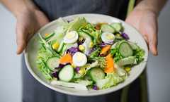 Two hands holding out a large plate of salad.