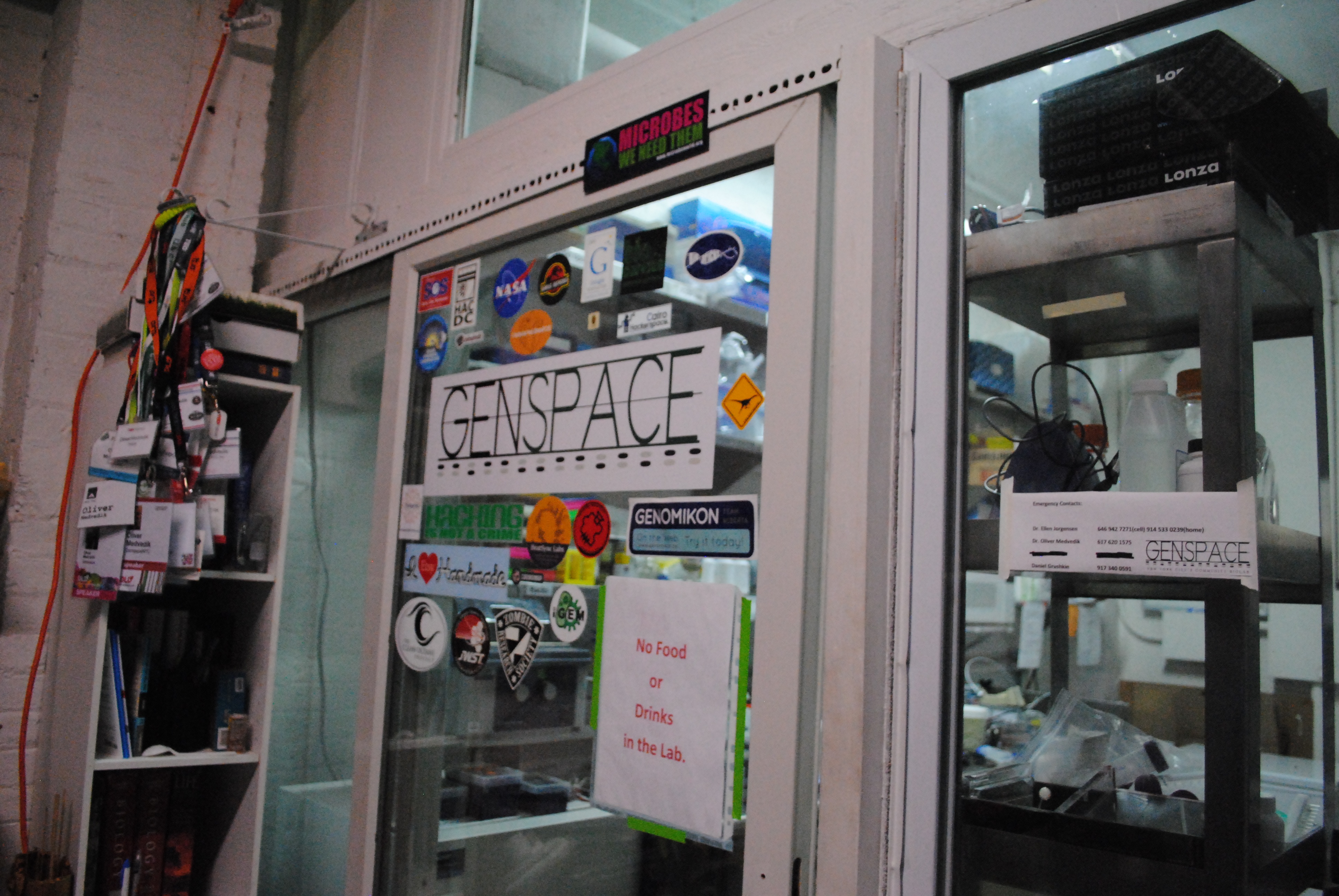 Lab entrace to GenSpace for DIY biohackers in New York. The entrance has glass windows covered with stickers and a sign that restricts food and drinks. Behind the entrance lies lab equipment,