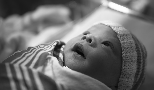 Grayscale close up of a child looking wide-eyed as they lay bundled in blankets.