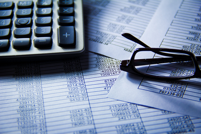 A calculator and eye glasses rest on piles of paper