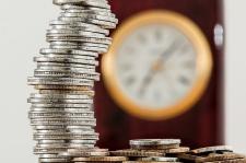 A clock is featured in the background of a stack of coins.