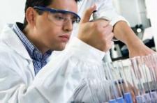 A person in a white lab coat pipettes liquid into test tubes