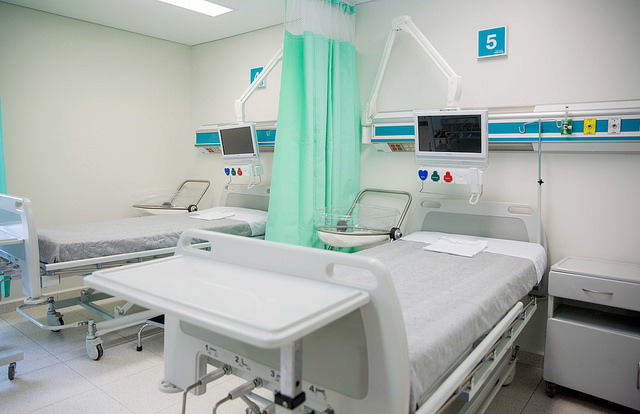 An empty hospital room, with two beds and screens, separated by a curtain