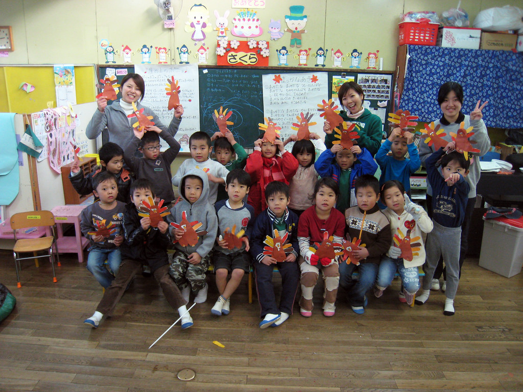 Class of kindergartners and three teachers holding up paper turkeys