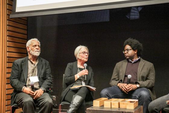 Seated, from left to right: Panelists Troy Duster, Rosemarie Garland-Thomson, and Osagie Obasogie holding microphones. Garland-Thomson holds her microphone up as she speaks.