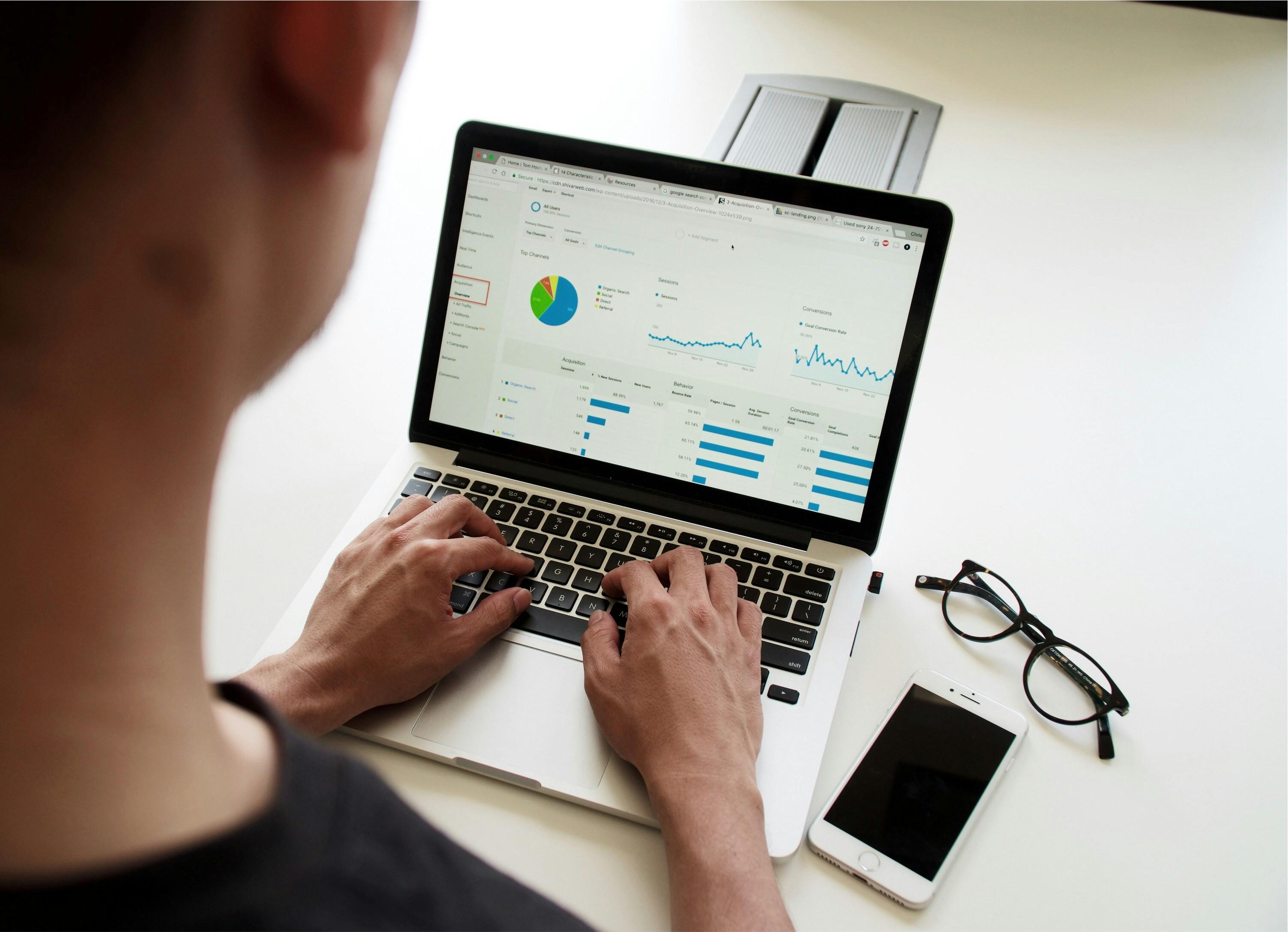 Man is shown typing on his laptop analyzing various data visualizations, such as pie charts, line graphs and bar graphs.