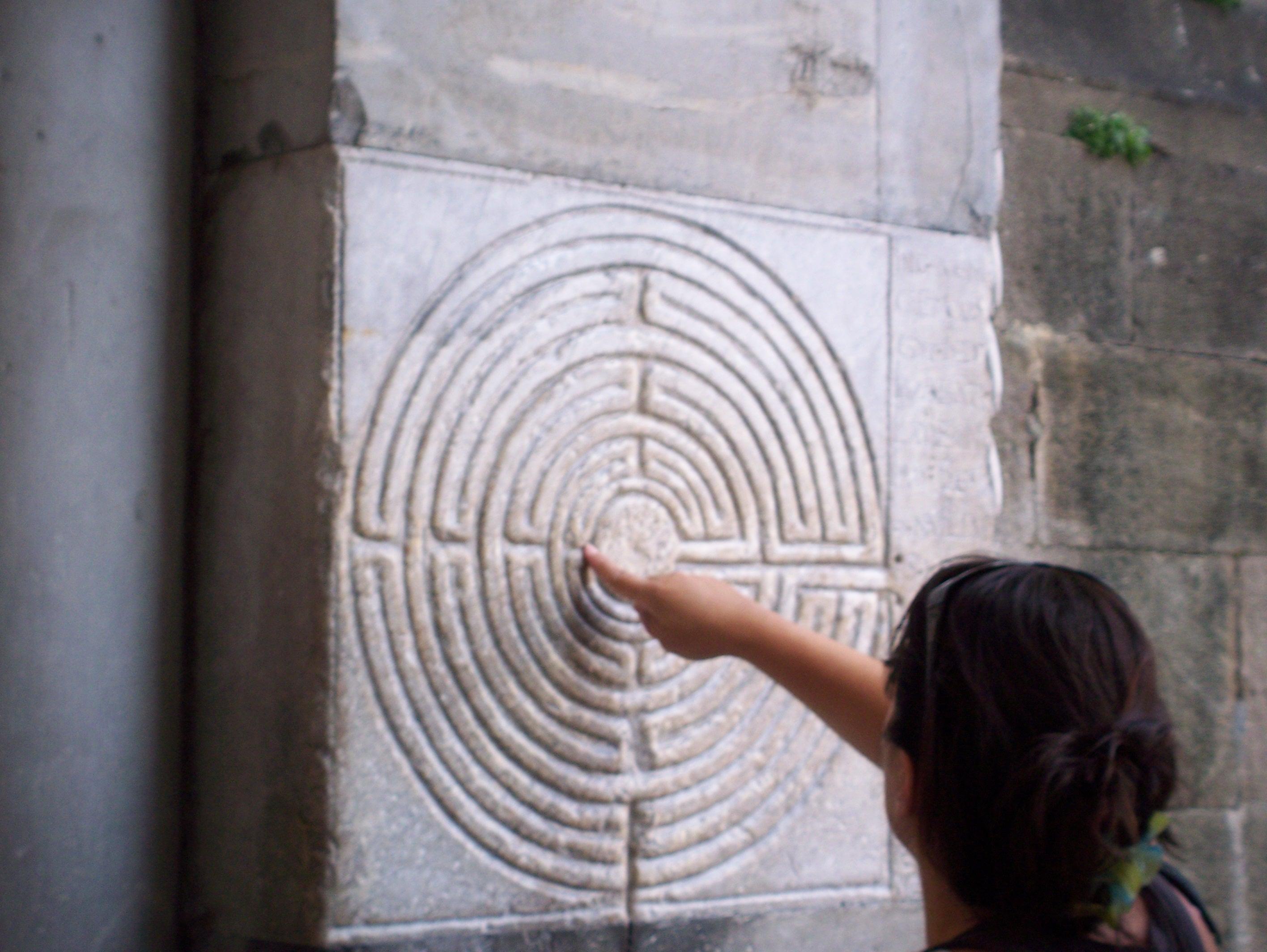 A person faces a maze on the wall and uses their fingers to trace a path within the maze.