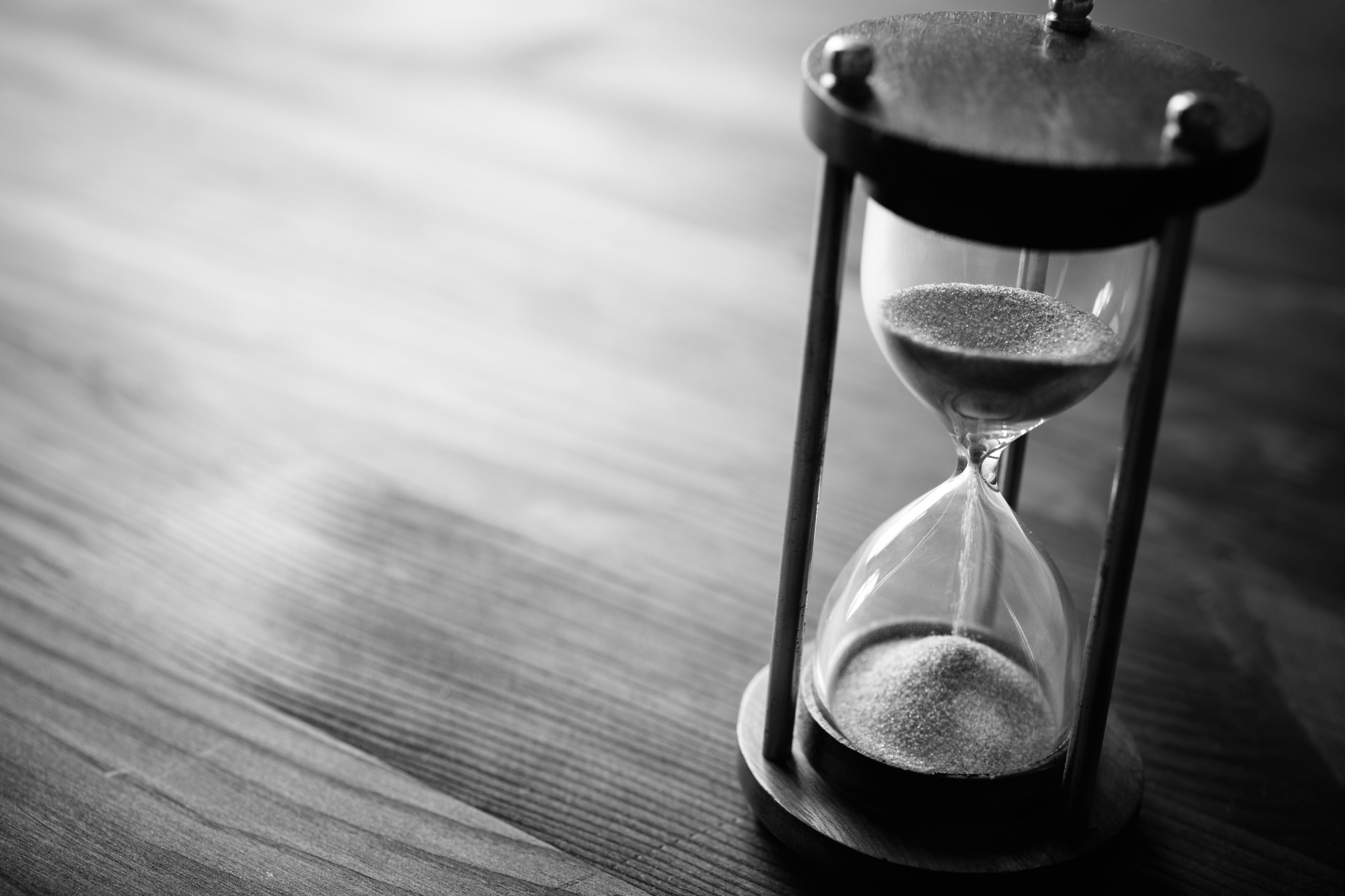 Black and white photo of an hour glass, with sand falling.