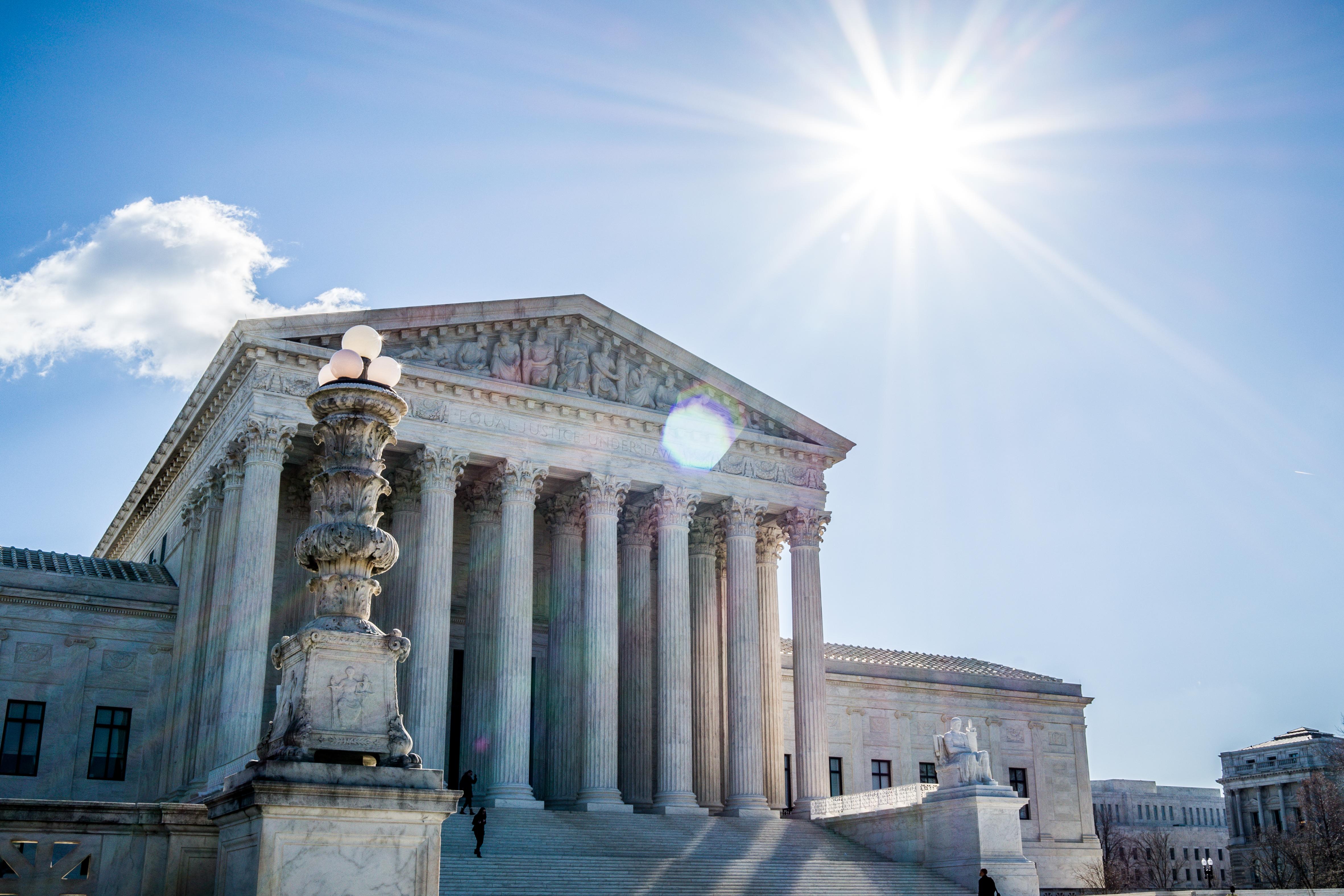 Landscape photo of the US Supreme Court building. with the sun and blue sky above.