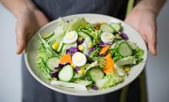 Two hands holding out a large plate of salad.