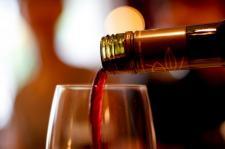 Wine is poured over the top of a wine glass. Background is left unfocused with lights.