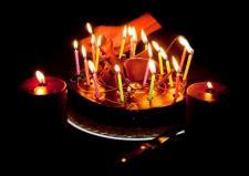 In a darkened room, several candles are lit on top of a birthday cake.