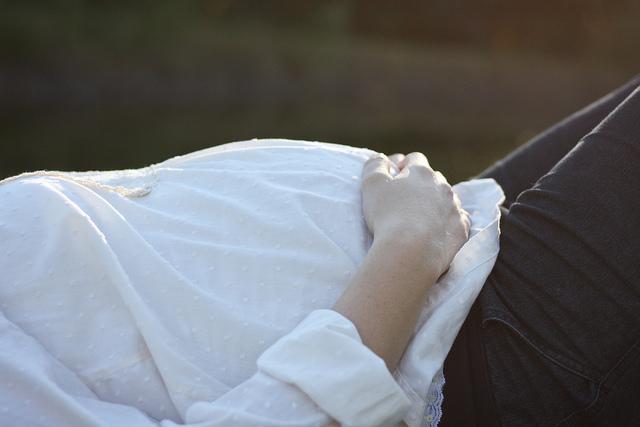 A woman's torso is shown laying on her side. She wears a white shirt and black pants. Hand is gently placed on the bottom of stomach.