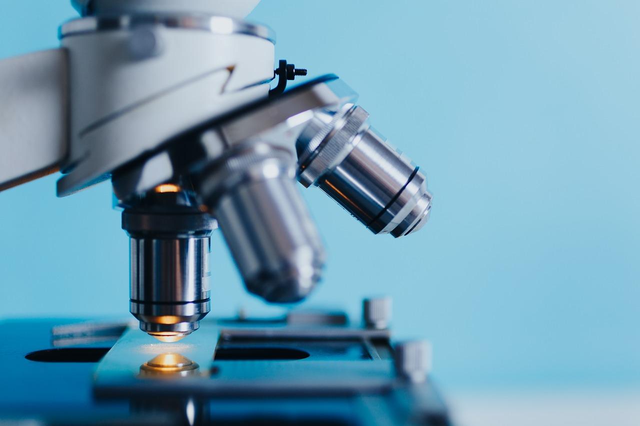 A close up shot of a lab microscope with one of three focal heads pointed at a piece of glass and sample below.