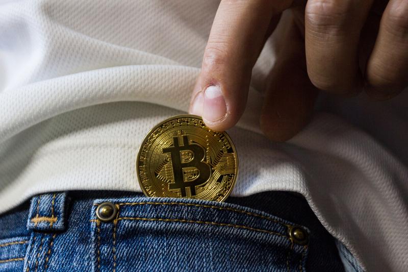 fingers pulling a bitcoin out of jeans pocket