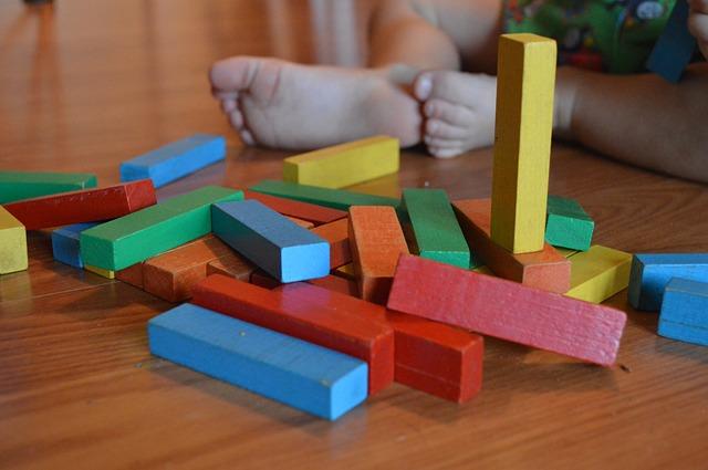 Several baby blocks are scattered on a hardwood floor, with a baby's feet in the background.