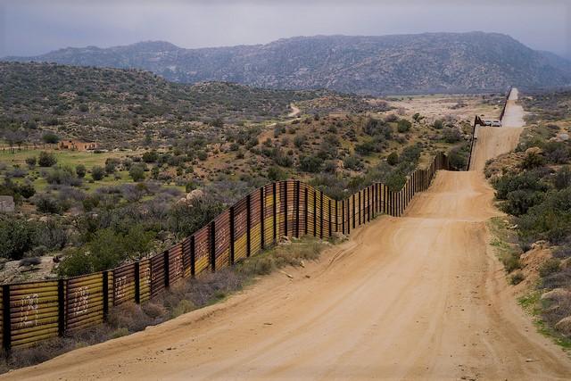 Lonely road stretching into the distance with the U.S. Mexico border wall flanking it.