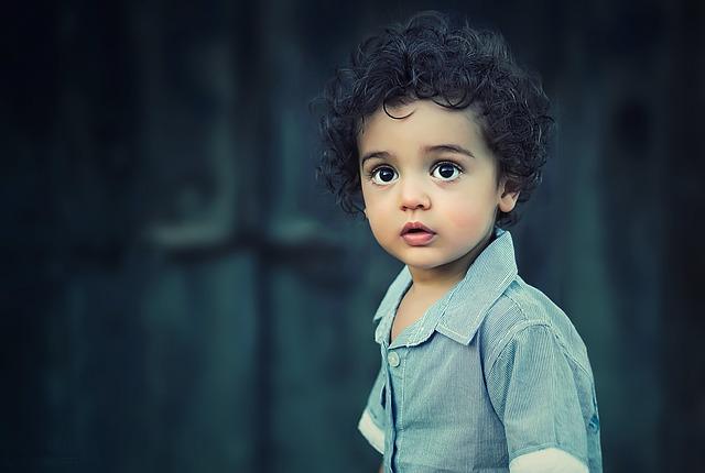 Child with curly hair and a blue button-down shirt staring above and to the left of the camera.