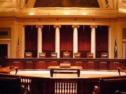 Large, empty wooden court room. 4 columns are across the wall behind the stand.