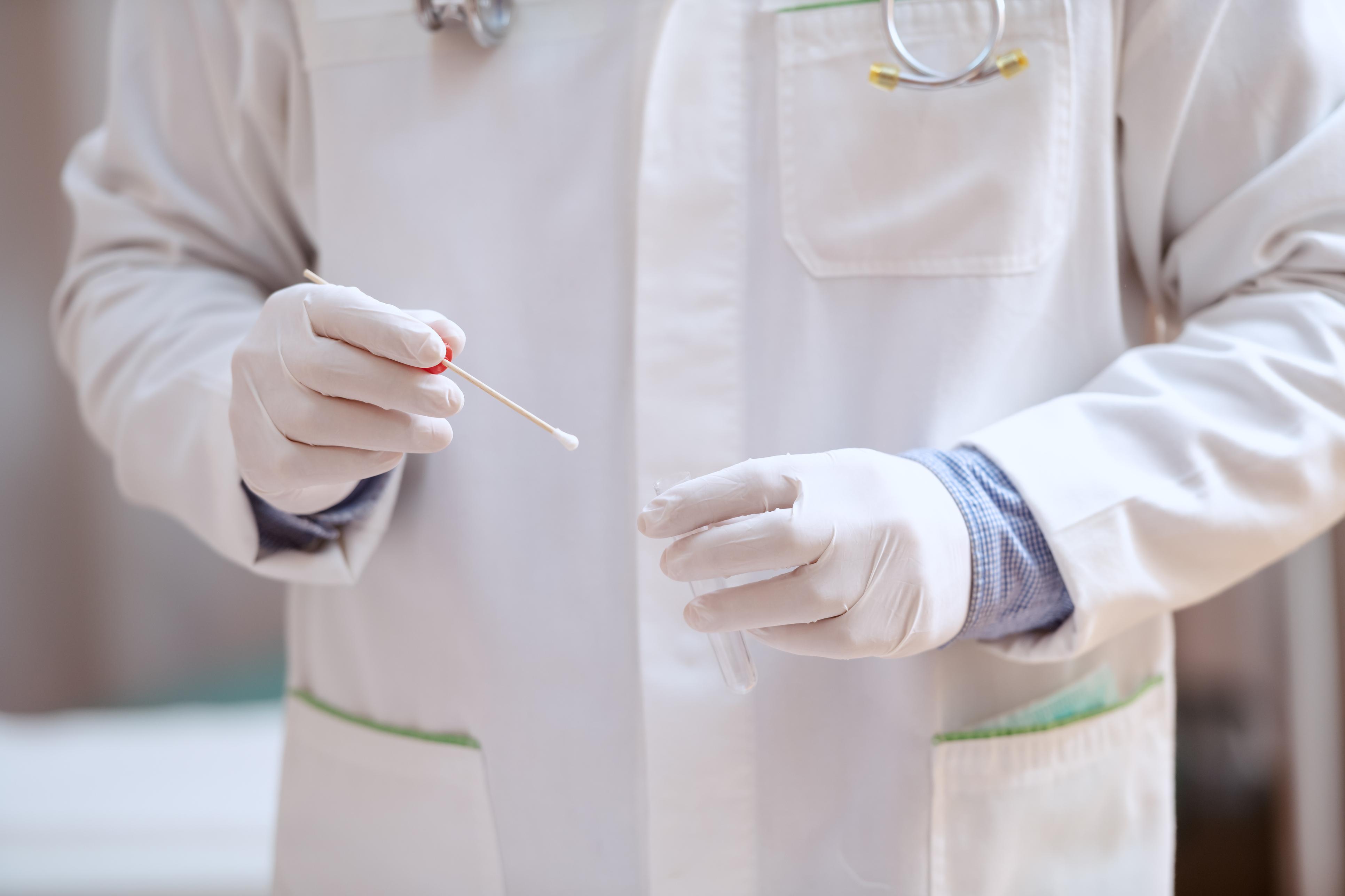 person in white lab coat holds swab