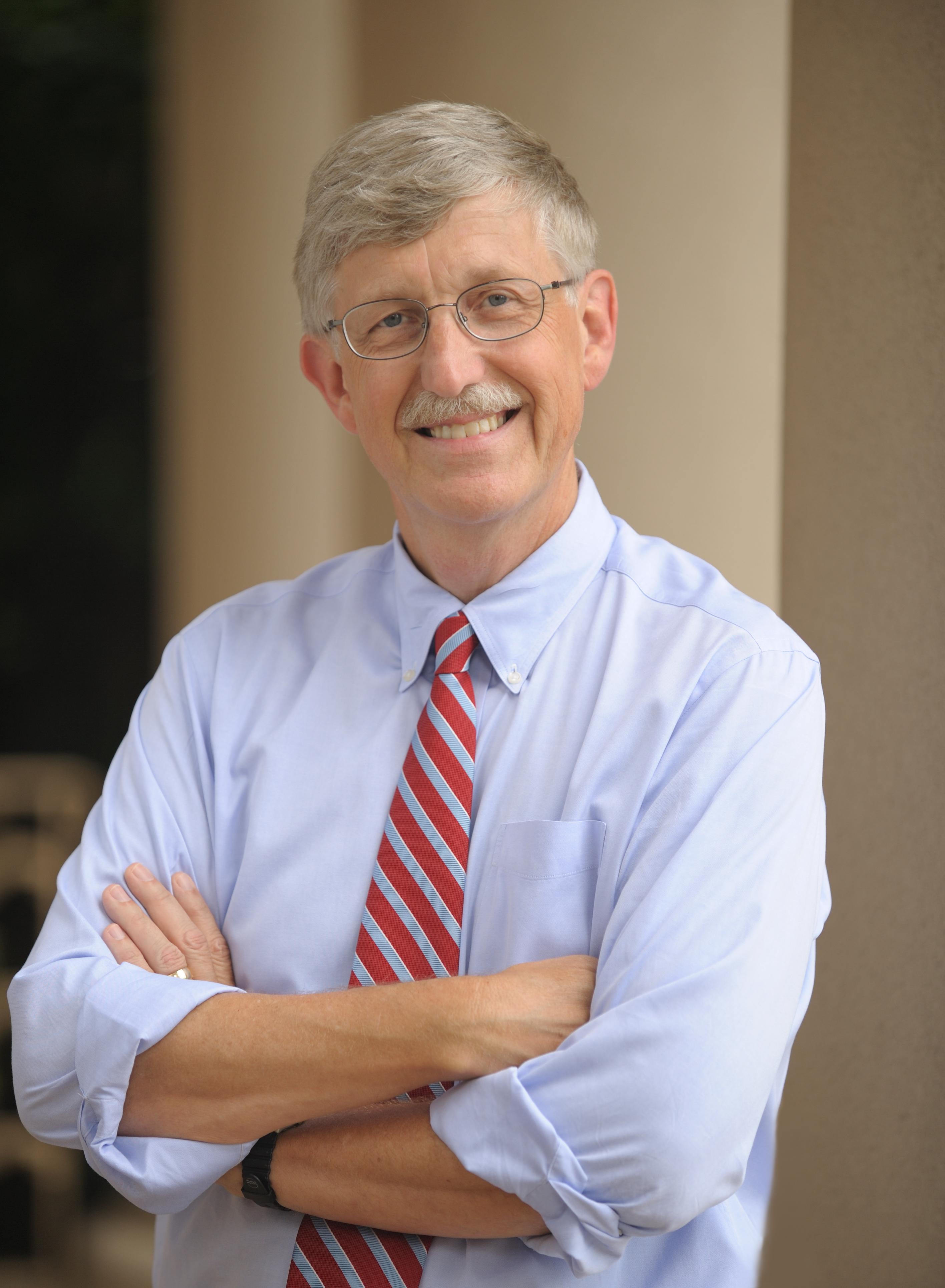 photo of a white man with grey hair and mustache, crossing his arms and smiling