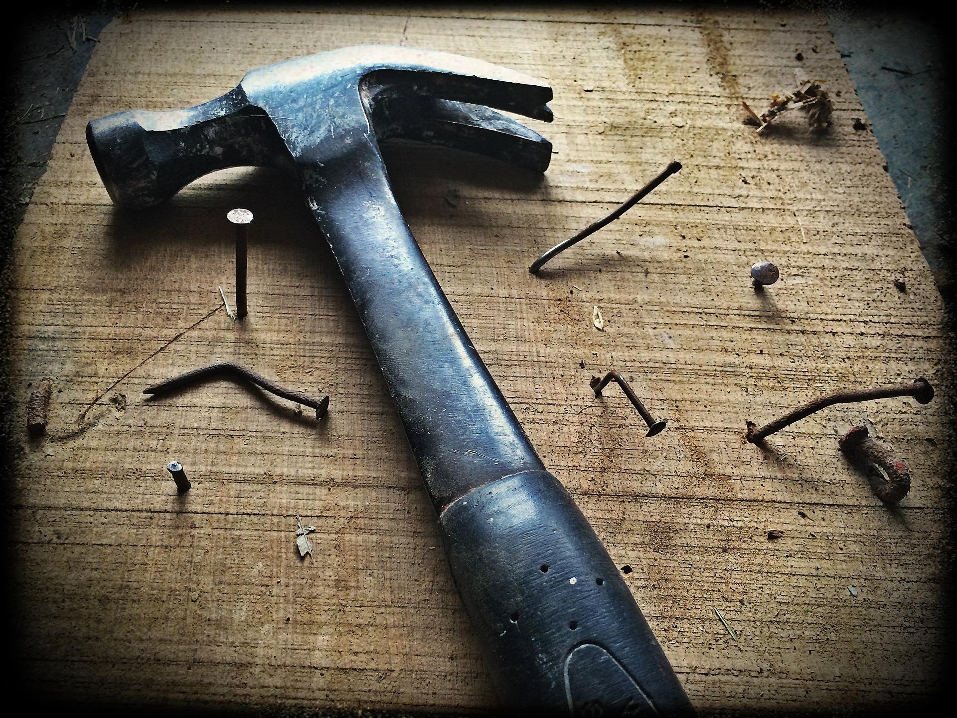 A hammer is shown in the middle, with several nails attached to a wooden board. The nails are dented and bent.