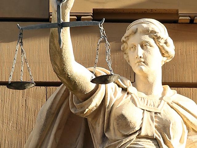 Close up of a statue of Themis, the Greek Goddess of Justice, holding a scale in one hand. Sunshine falls and creates shadows in the statue crevices.