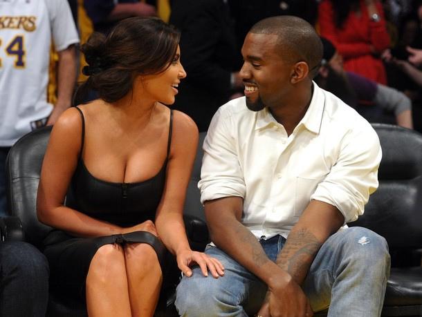 In the front row of a basketball game, Kim Kardashian and Kanye West look at each other, engaged in an amusing conversation