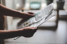 An individual sits, reading a newspaper/