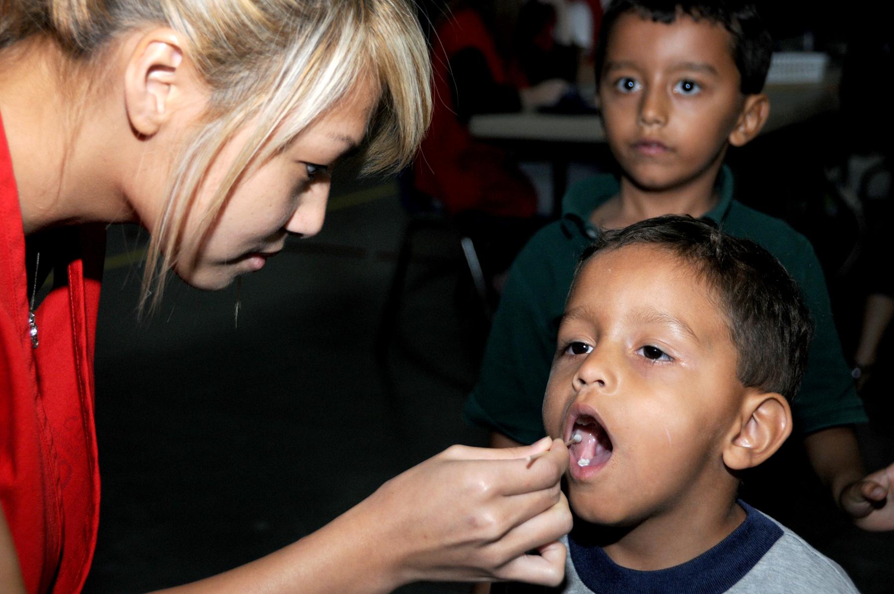 Child getting his mouth swabbed by woman wearing red scrubs