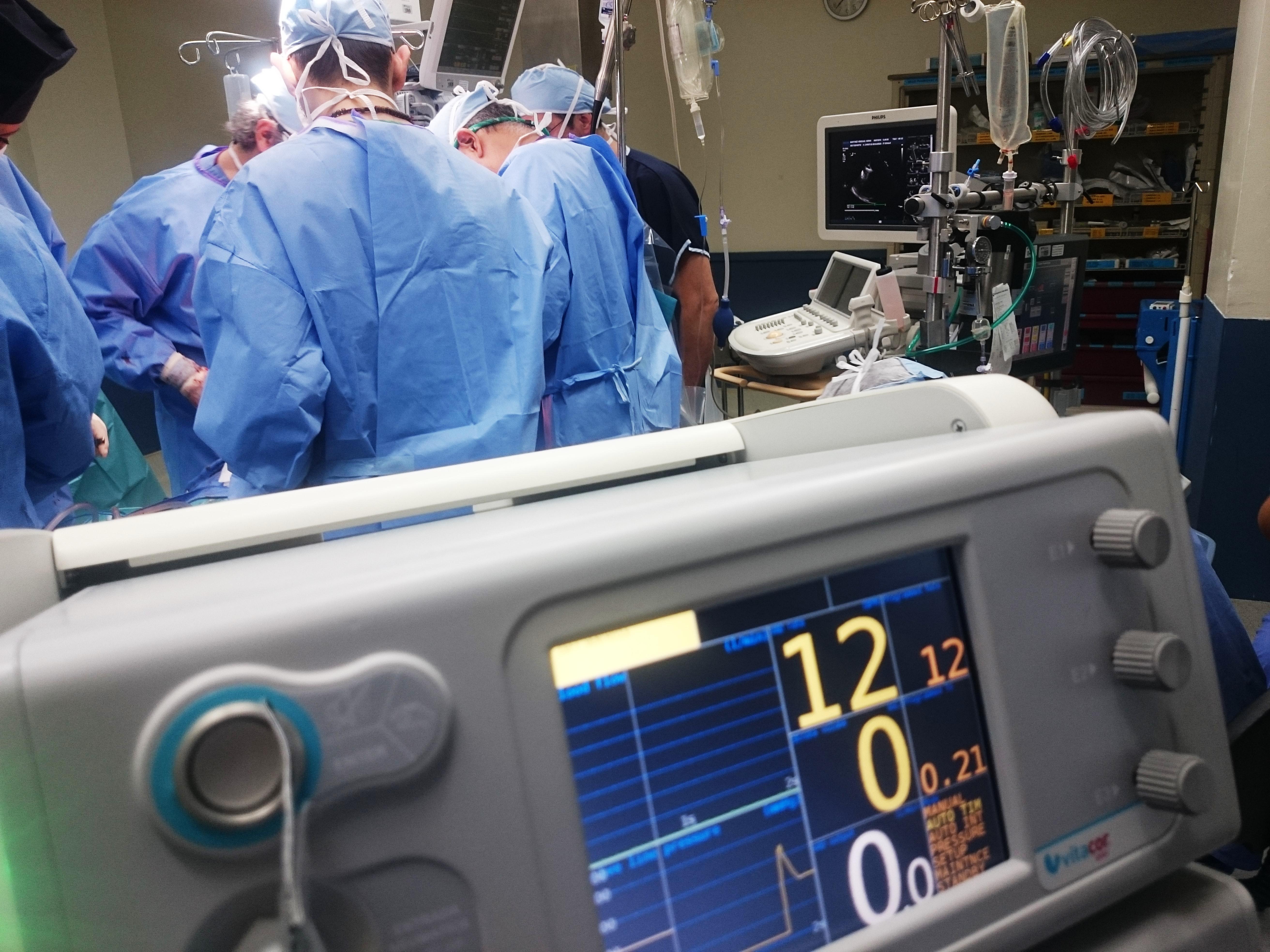 Hospital room with monitor in the foreground, blue-gowned figures in the background