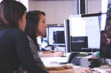 Two women view a computer desktop, appearing to be working.