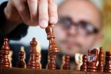 The picture is focused on a wooden chess game, with an individual in the background.