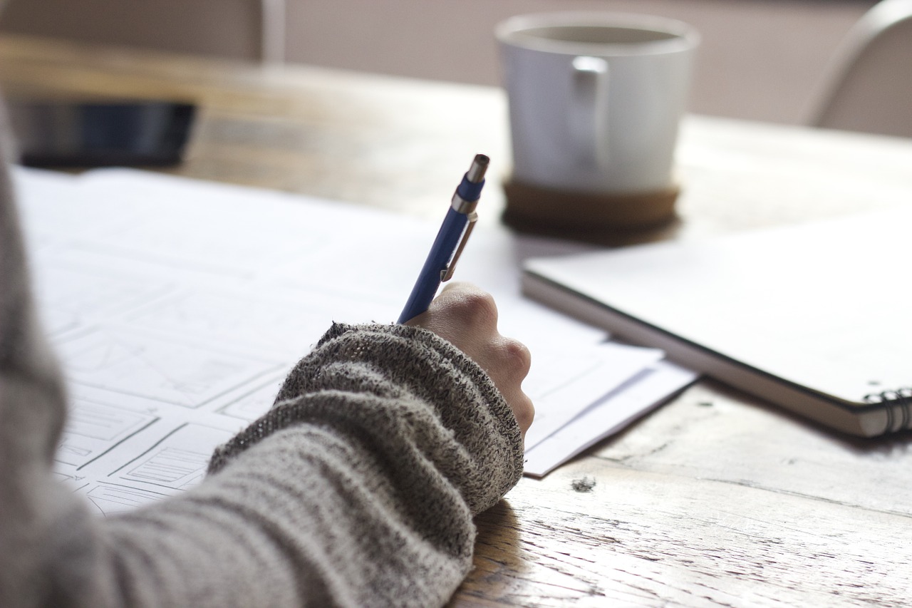 A close-up on a hand with a pen writing on pieces of paper on a desk. 